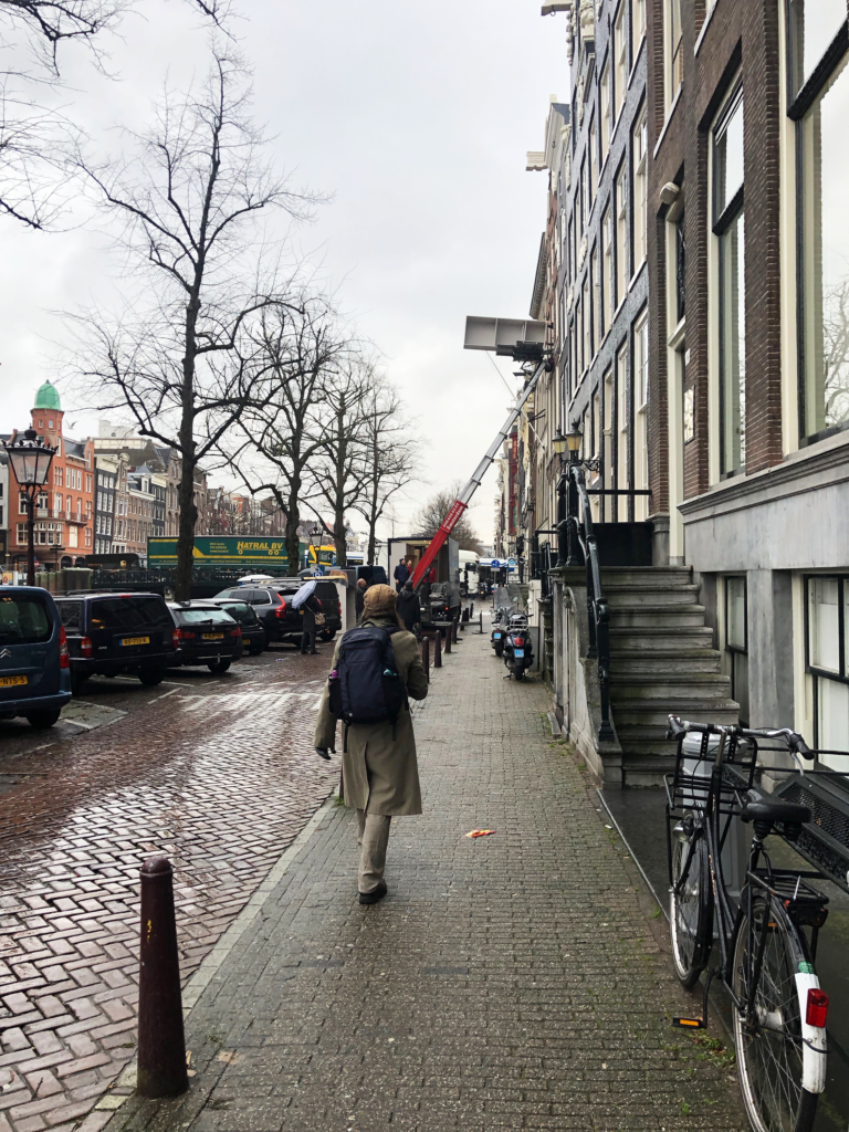 A photo of a man walking down a canal street in Amsterdam, toward a truck with an extended ladder for lifting furniture into open windows