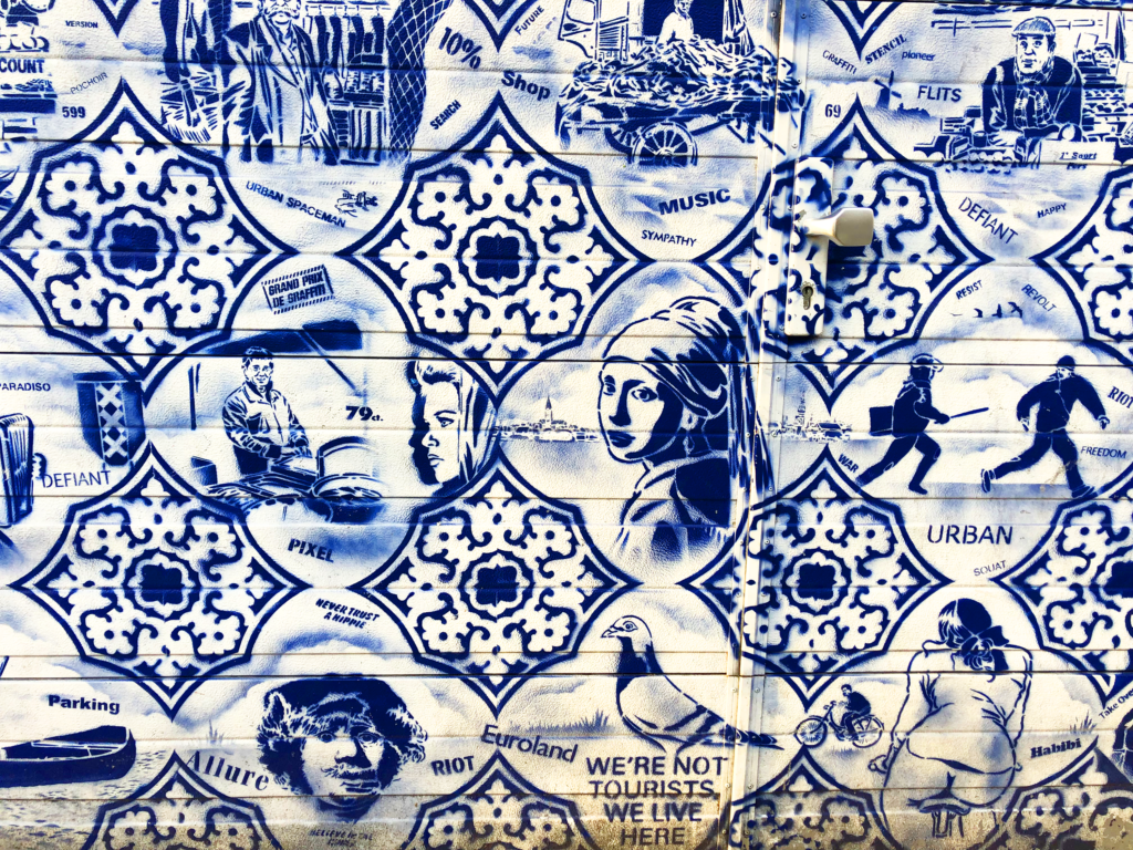 A photo of blue-and-white stenciled graffiti with a pigeon, a woman on a bike, the Girl with Pearl Earring, and other scenes from Amsterdam