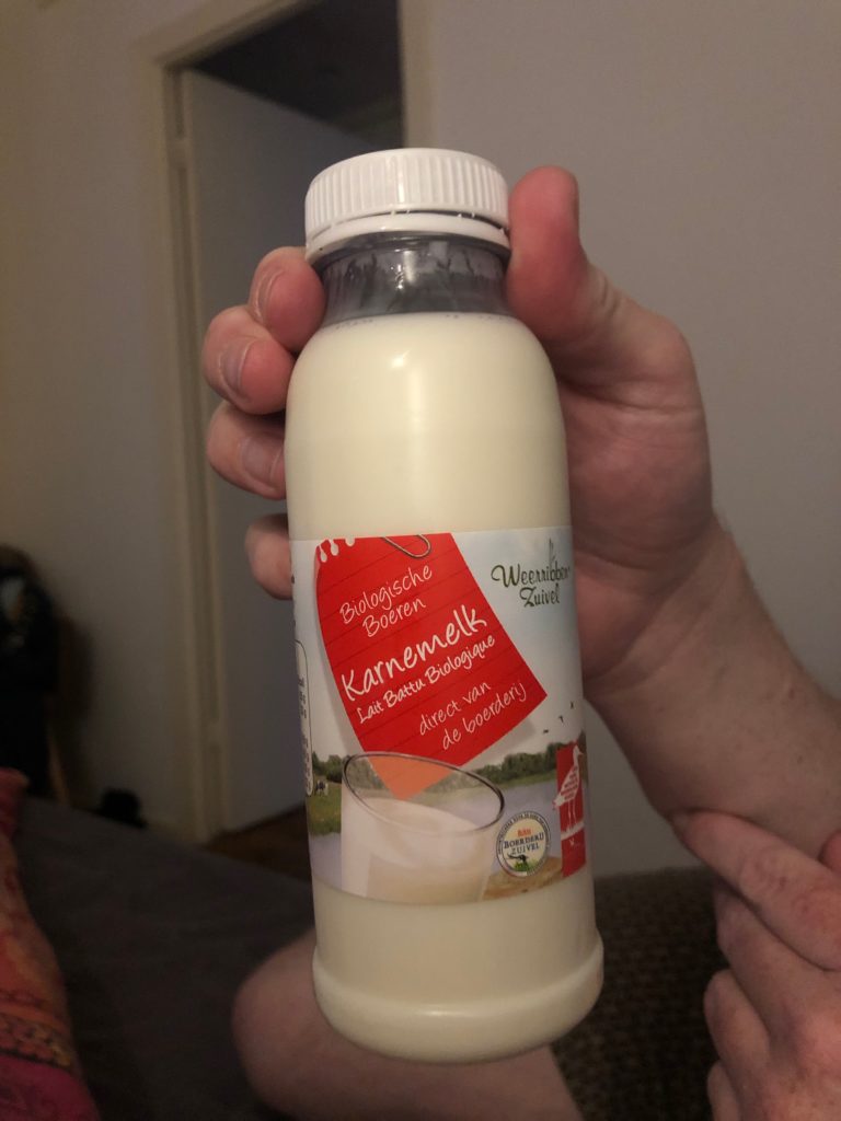 A photo of a white person's hand holding a plastic bottle of karnemelk (buttermilk)