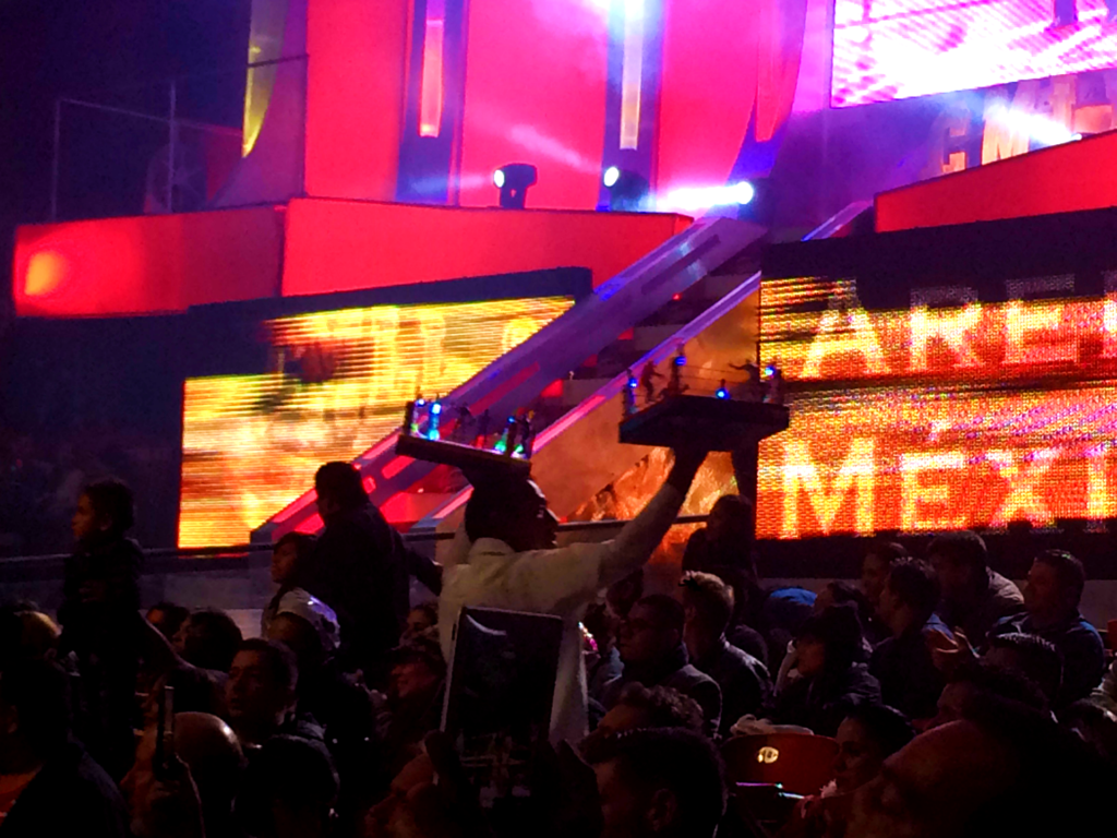 A vendor in a crowd at a lucha show sells a tiny lucha wrestling ring