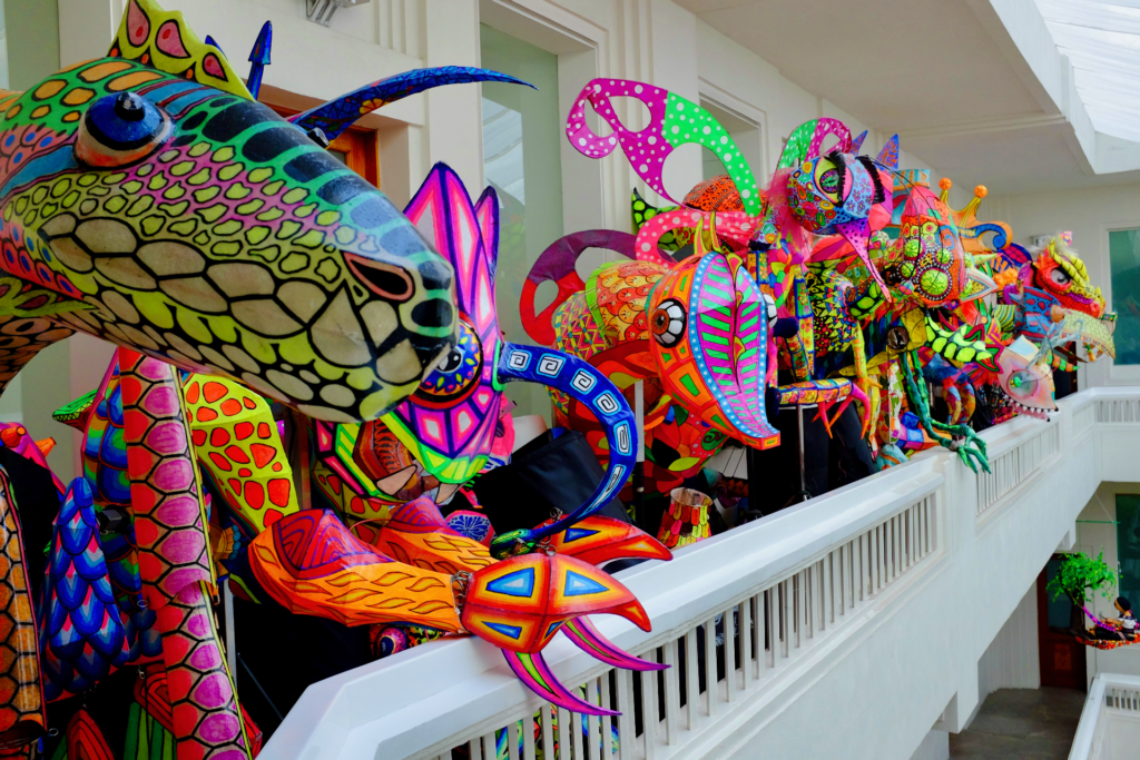 Several human-sized brightly colored alebrije sculptures made with paper, gathered on a white balcony at the Museo Artes Populares