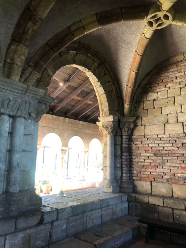 Brick walls and arches, light shining through behind them, at the Cloisters in New York