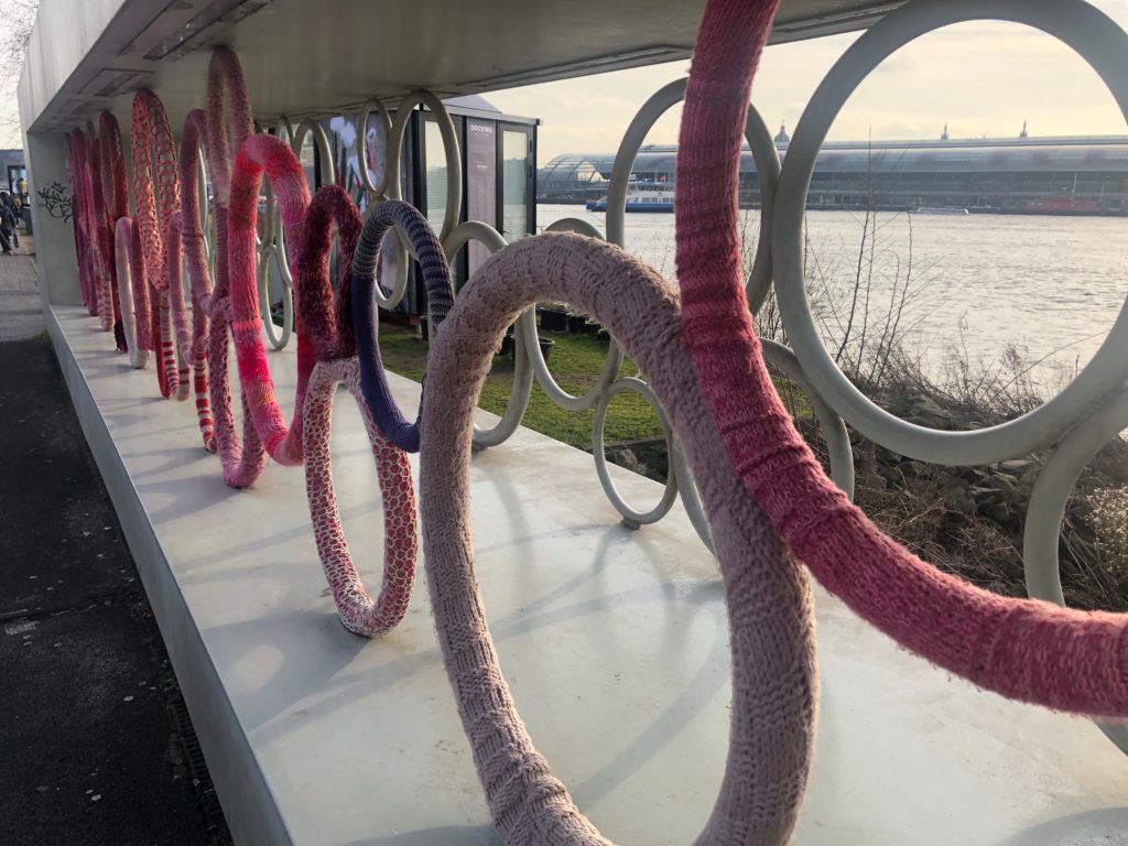 Yarn-bombed sculpture of rings in front of the north Amsterdam waterfront