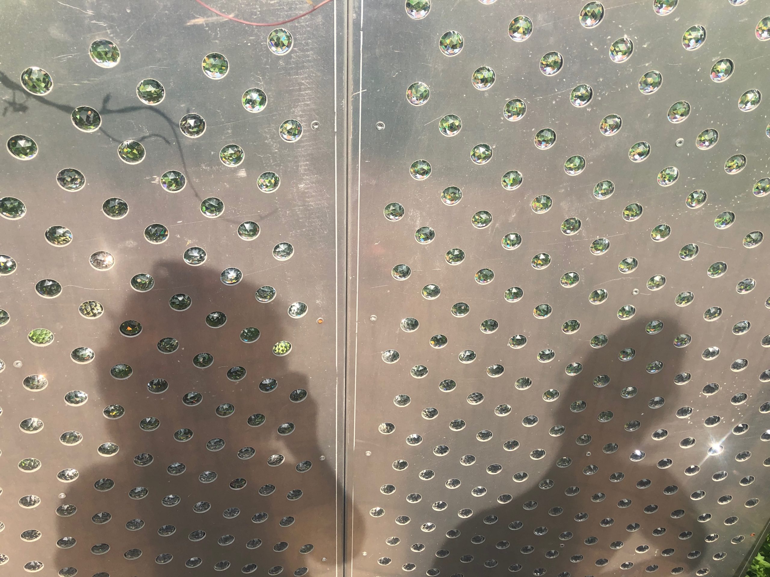 a silver metal surface studded with faceted pieces of clear glass, and two people's shadows on it