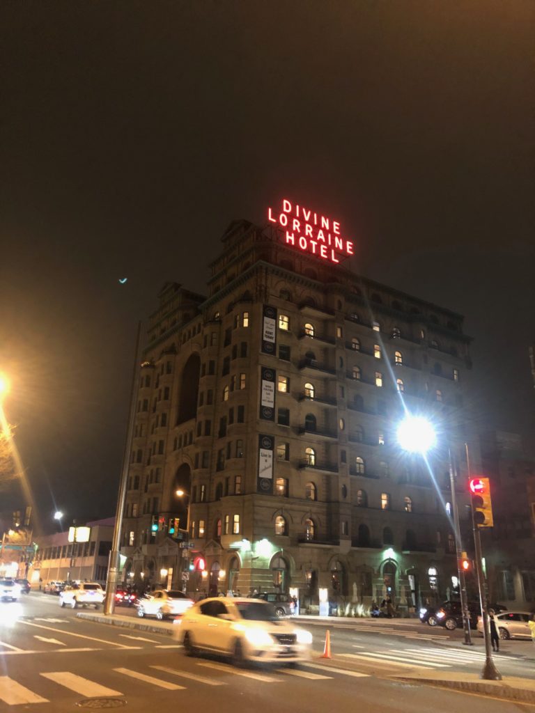 A ten-story building on a street corner, at night, a red neon sign on top reading "Divine Lorraine Hotel"
