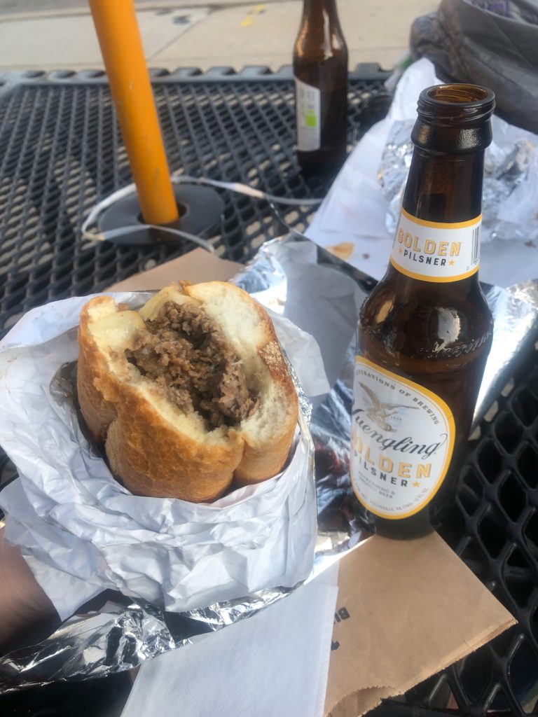 An open bottle of Yuengling beer with a cheesesteak sandwich sticking out of foiled paper.