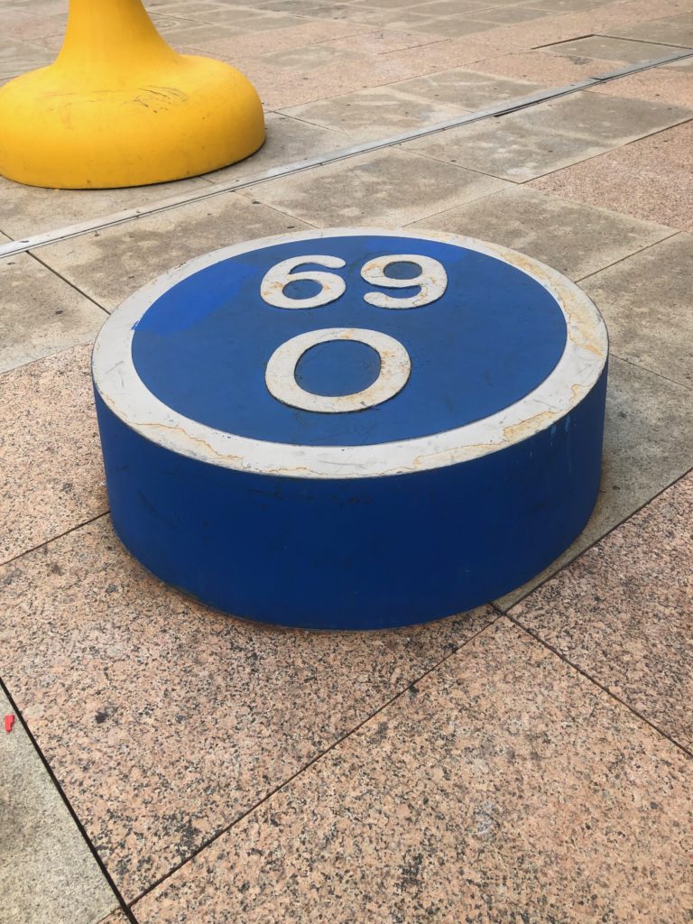 A large game piece, blue and round with white writing saying O-69, sitting on granite tiles outside