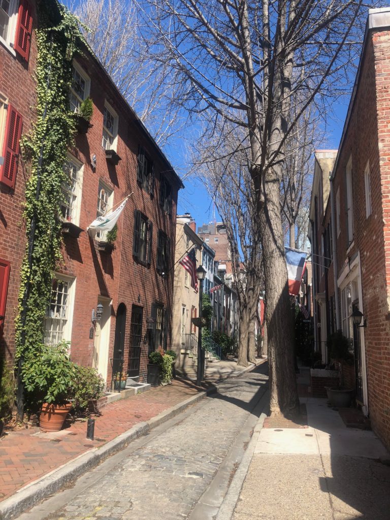 A Philadelphia street with old brick houses, a narrow cobblestone lane, trees, and gaslamps