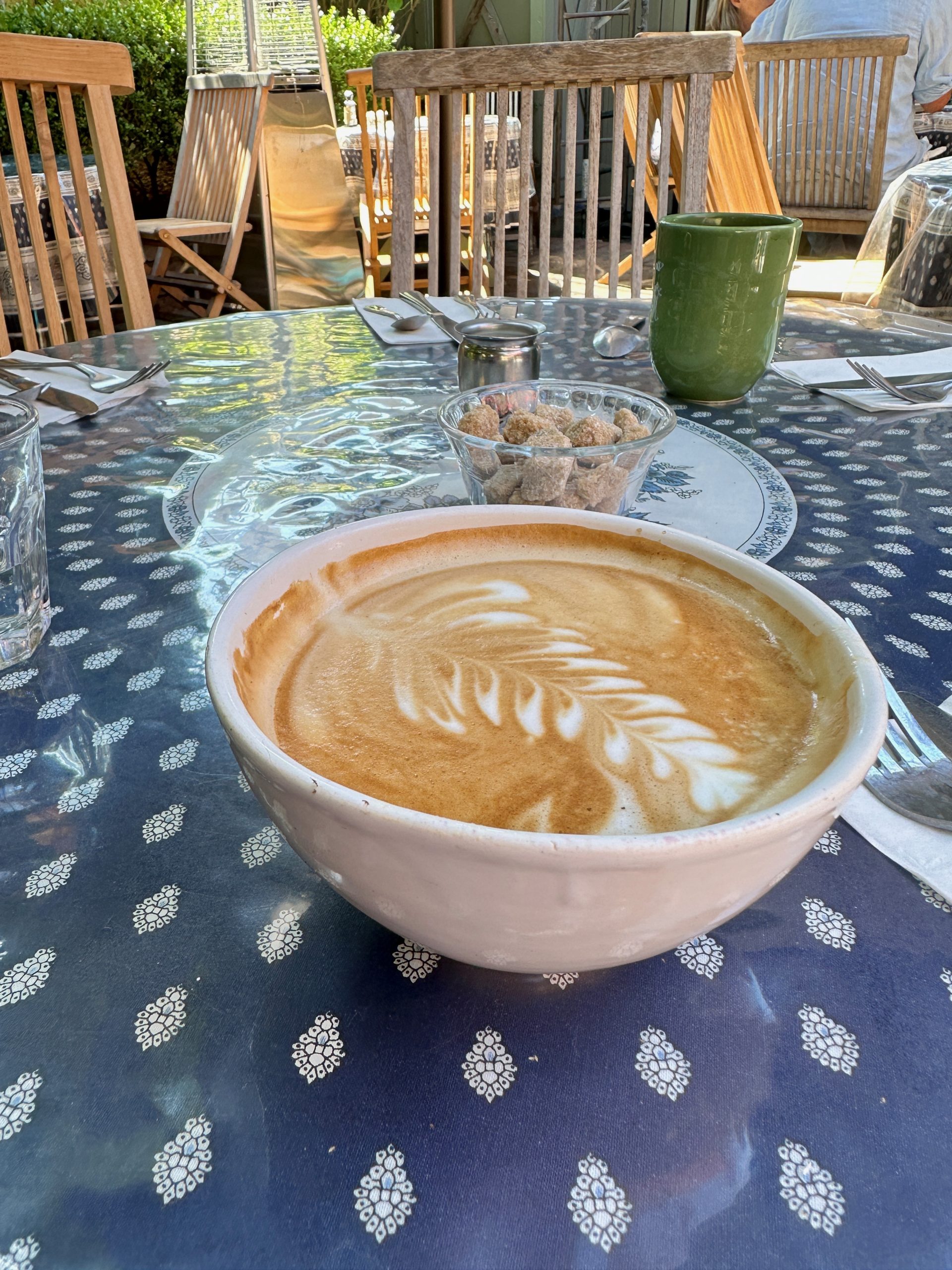 A fancy latte in a bowl with a feather design on the foam atop a patterned blue-and-white tablecloth